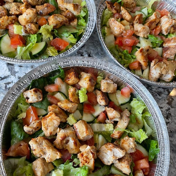 Three Roscoes Eatery chicken salads in foil containers, with lettuce, tomatoes, cucumbers, and grilled chicken.
